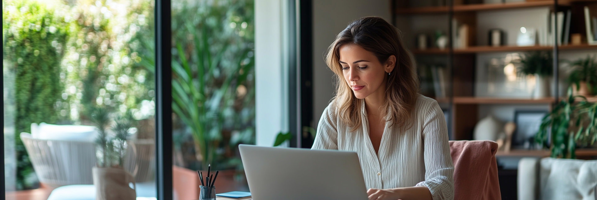 Femme travaillant sur ordinateur dans un bureau lumineux ouvrant sur un patio verdoyant