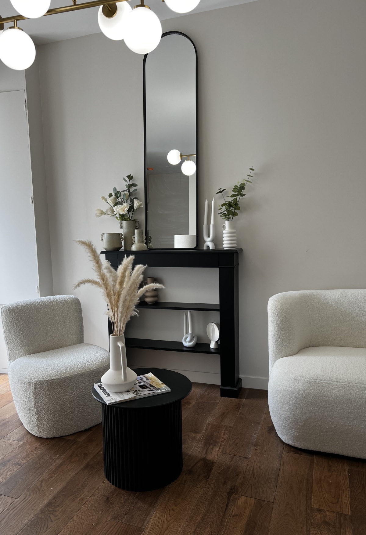 Salon minimaliste blanc, fauteuils bouclé et console noire avec miroir arqué